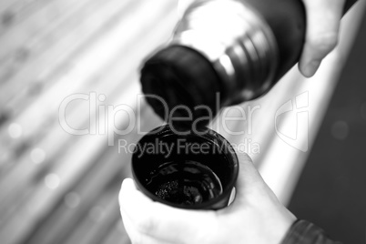 Filling cup with hot tea from thermos bokeh background