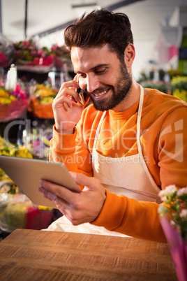 Male florist talking on mobile phone while using digital tablet