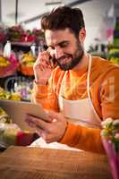 Male florist talking on mobile phone while using digital tablet