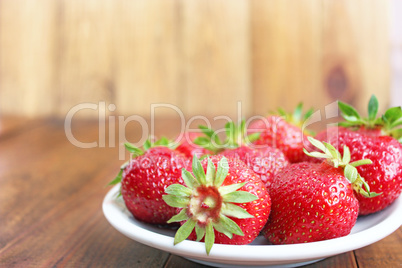 ripe red strawberries on the white plate on the brown