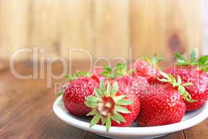 ripe red strawberries on the white plate on the brown