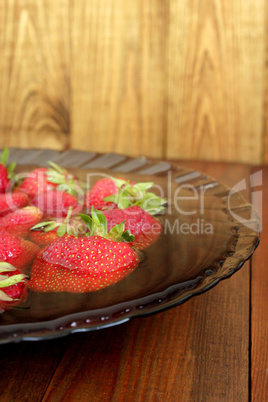 ripe red strawberries in the water on the plate on the brown