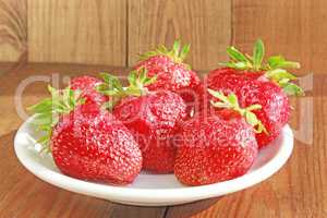 ripe red strawberries on the white plate on the brown