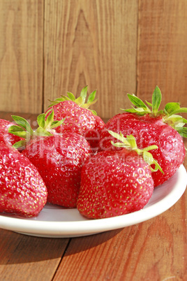 ripe red strawberries on the white plate on the brown