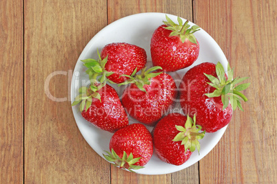 ripe red strawberries on the white plate on the brown