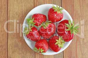 ripe red strawberries on the white plate on the brown