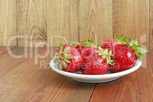 ripe red strawberries on the white plate on the brown