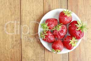 ripe red strawberries on the white plate on the brown