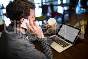 Man holding disposable coffee cup while talking on mobile phone