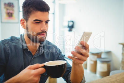 Young man text messaging on mobile phone while having coffee