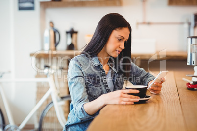 Young woman text messaging on mobile phone while holding coffee