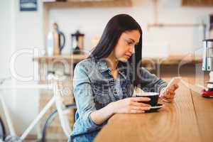 Young woman text messaging on mobile phone while holding coffee