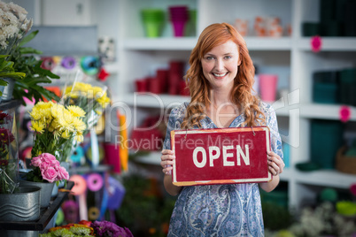 Smiling florists holding open sign placard in flower shop