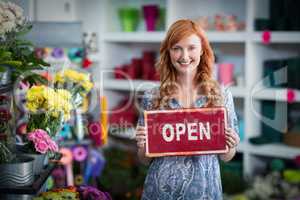 Smiling florists holding open sign placard in flower shop