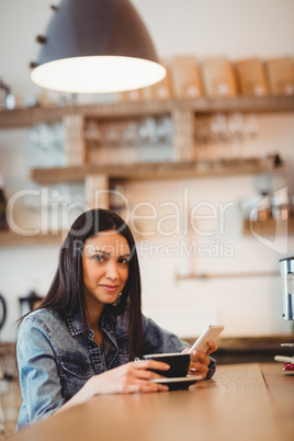 Young woman holding mobile phone and coffee cup