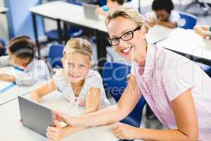 Schoolgirl and teacher using digital tablet in classroom