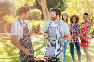 Men holding a beer bottle while preparing barbecue grill