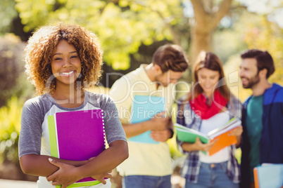 Portrait of college girl holding notes with friends in backgroun