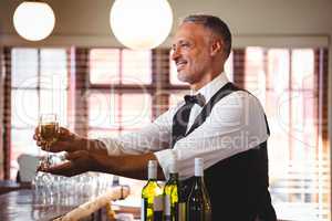 Smiling bartender offering a glass of wine at bar counter