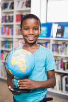 Schoolboy holding globe in library