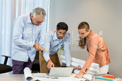 Businesswoman and coworkers discussing blueprint using laptop