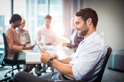 Man using digital tablet while coworker interacting in the backg
