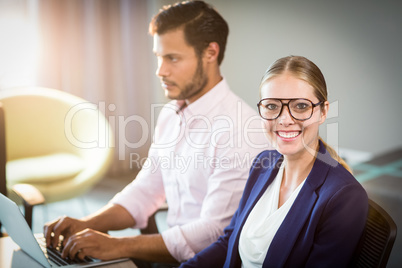 Businesswoman smiling at camera while her colleague using laptop