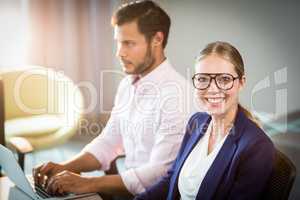 Businesswoman smiling at camera while her colleague using laptop