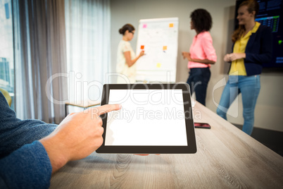 A colleague using digital tablet while coworkers discuss flowcha