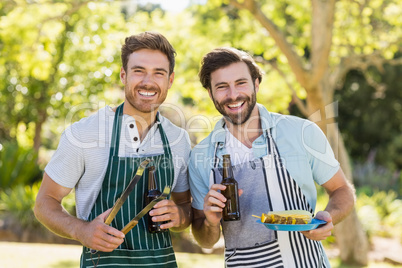 Portrait of two happy men holding barbecue meal and beer bottle