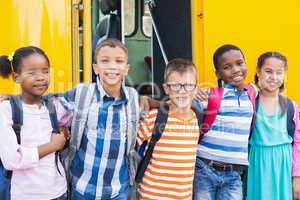 Smiling kids standing arm around in front of school bus
