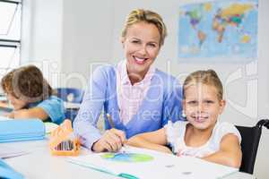 Teacher helping schoolgirl with her homework in classroom