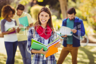 Portrait of college girl holding notes with friends in backgroun