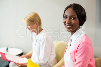 Woman smiling at camera while her colleague reading document