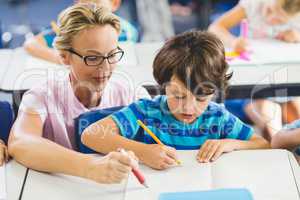 Teacher helping a boy with studies in classroom