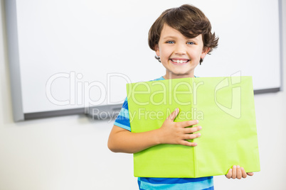 Portrait of schoolboy standing with book in classroom