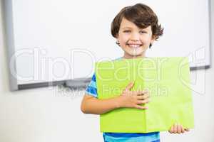 Portrait of schoolboy standing with book in classroom