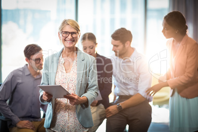 Businesswoman holding digital tablet while coworker interacting