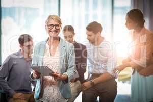 Businesswoman holding digital tablet while coworker interacting