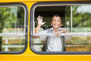 Smiling schoolboy waving hand from bus