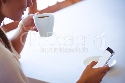 Woman using smartphone and drinking coffee