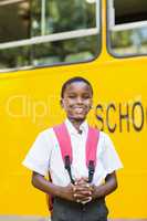 Smiling schoolboy standing in front of school bus