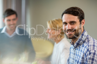 Man smiling at camera while colleagues interacting in the backgr