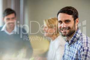 Man smiling at camera while colleagues interacting in the backgr