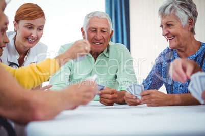 Smiling nurse and seniors people playing cards