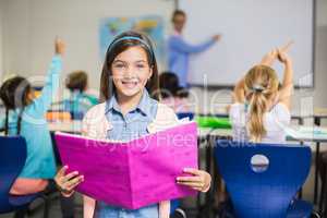 Portrait of schoolgirl standing with book in classroom