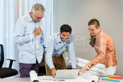 Businesswoman and coworkers discussing blueprint using laptop