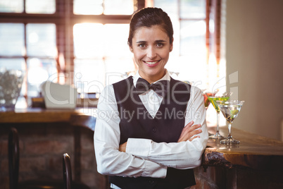 Smiling female bartender standing with arms crossed