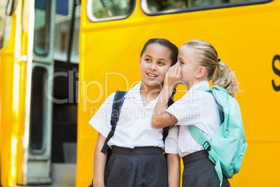 Smiling schoolgirl whispering in her friend's ear