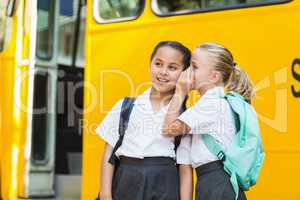 Smiling schoolgirl whispering in her friend's ear